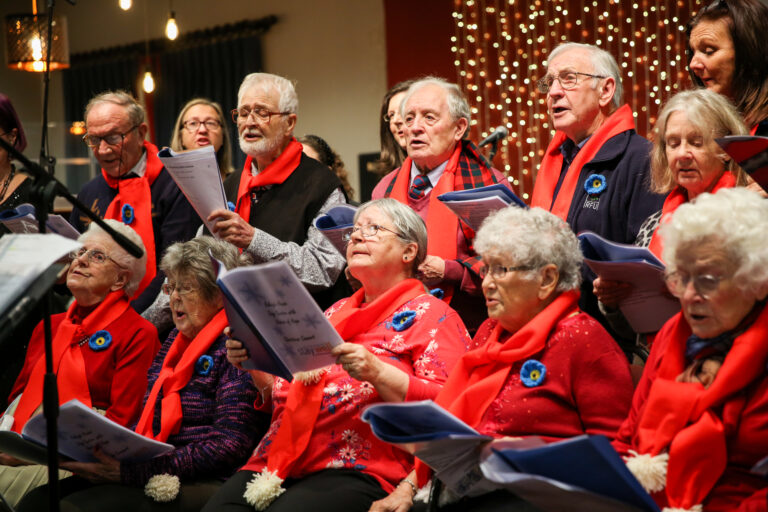 Members of our older people's choirs, wearing red and black, perform in a concert